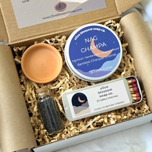 A gift set that includes a tin of incense cones, a terracotta incense burner, a tin of matches, and a glass vial of black lava sea salt. 