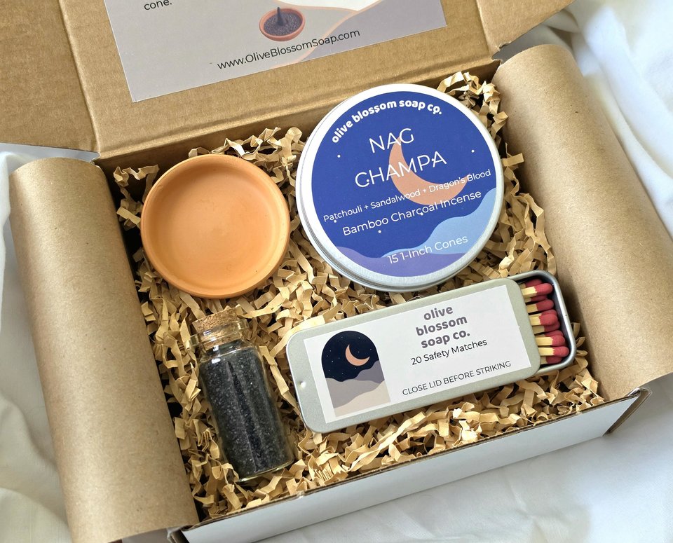 A gift set that includes a tin of incense cones, a terracotta incense burner, a tin of matches, and a glass vial of black lava sea salt. 