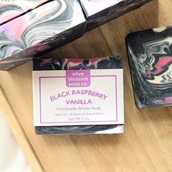 A swirled black, pink, purple, and white handmade bar on a wooden tray.