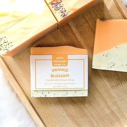An orange and white speckled bar of handmade soap resting on a wooden tray.
